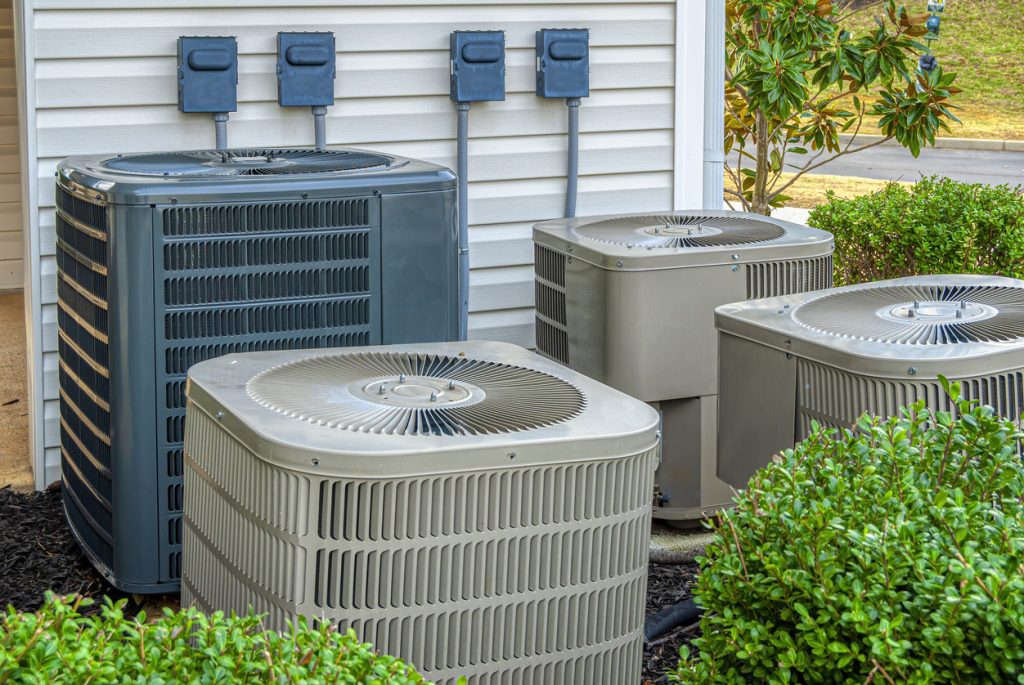 Horizontal shot of four air conditioning units outside of an upscale apartment complex.