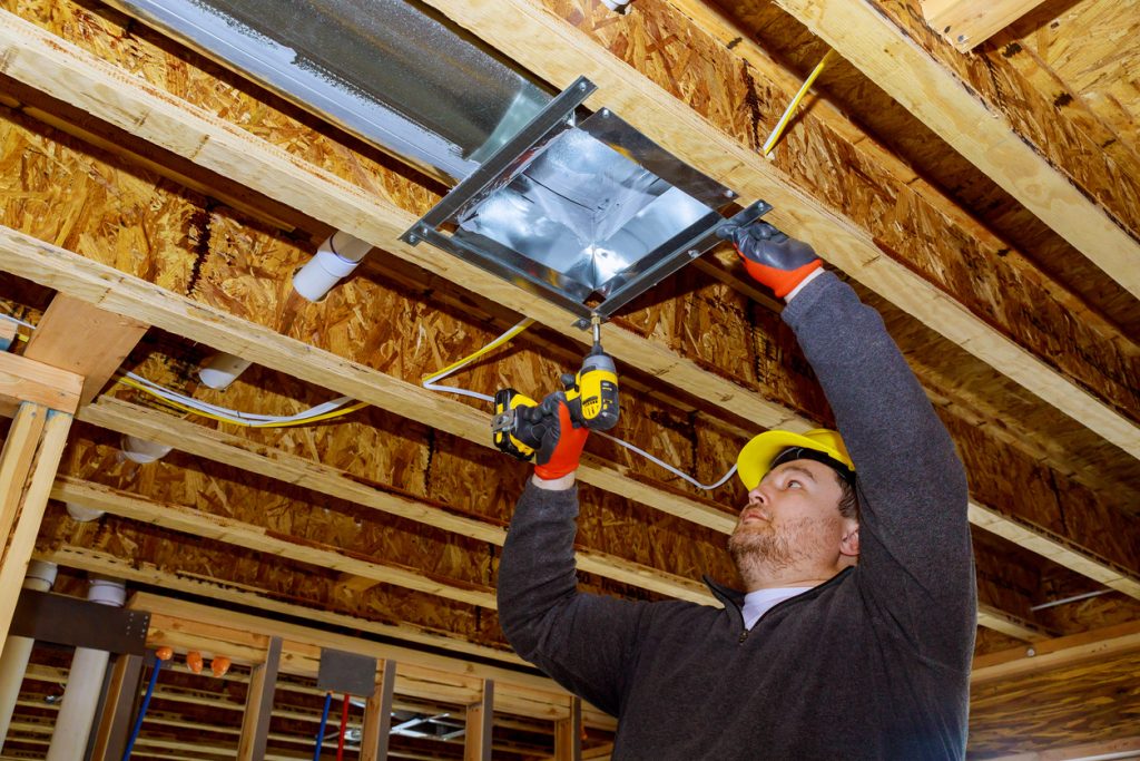 Male technician mounted air heating and cooling system on ceiling steel roof structure ventilation system