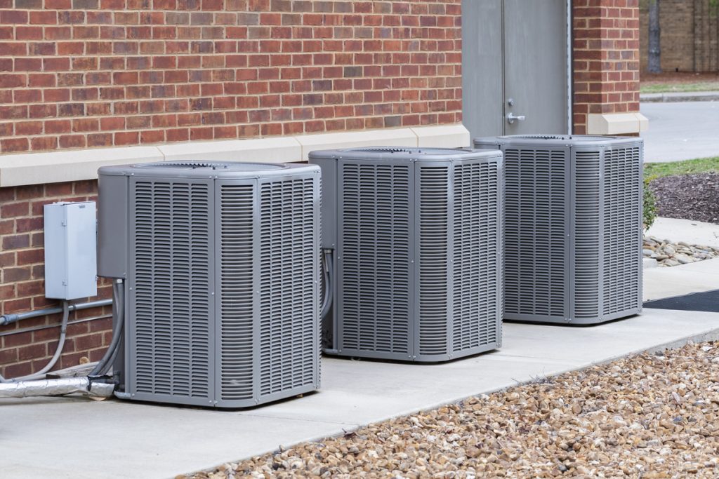 Horizontal shot of commercial air conditioners outside near a maintenance door.