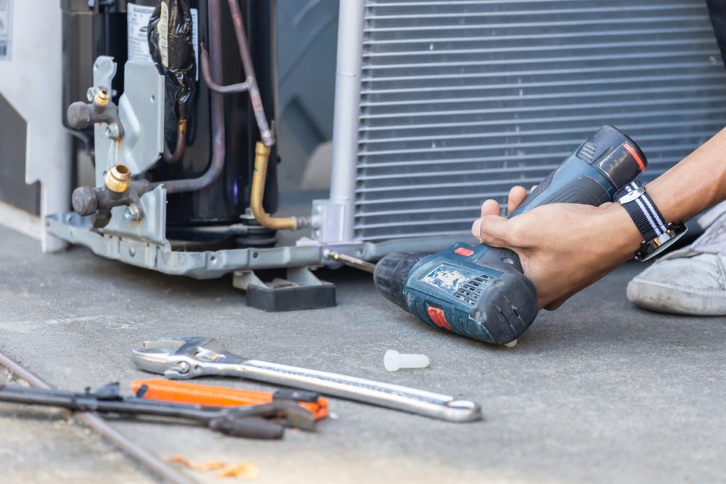 Selective focus Air Conditioning Repair, technician man hands using a screwdriver fixing modern air conditioning system